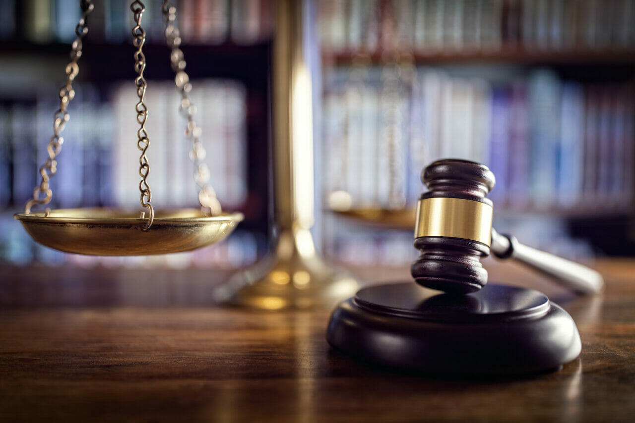Judge’s gavel and golden scales of justice on wooden desk in law library. Judge’s gavel and golden scales of justice on wooden desk in law library.