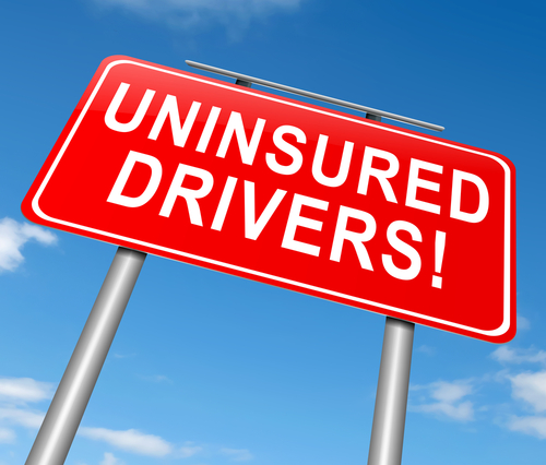 Bright red road sign with bold white text that says "UNINSURED DRIVERS" against a clear blue sky background.