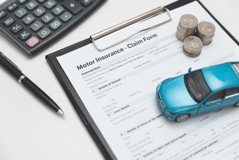 Motor insurance claim form with toy car, coins, pen, and calculator symbolizing auto accident claims and compensation. Motor insurance claim form with toy car, coins, pen, and calculator symbolizing auto accident claims and compensation.