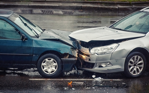 Two cars involved in a front-end collision on a wet road, showing visible damage to the front bumpers and hoods.
