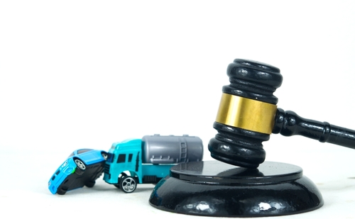 A judge's gavel beside two toy vehicles involved in a simulated collision, representing legal action after a truck accident.