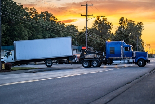 A large blue semi truck making a wide turn onto a road at sunset, with a white box trailer in tow.