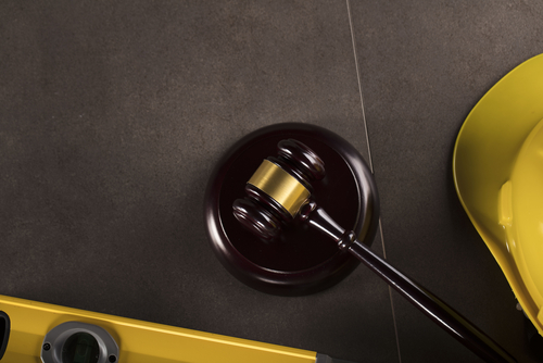Judge's gavel next to a yellow hard hat and level tool on a dark surface, symbolising legal issues in construction or workplace safety.