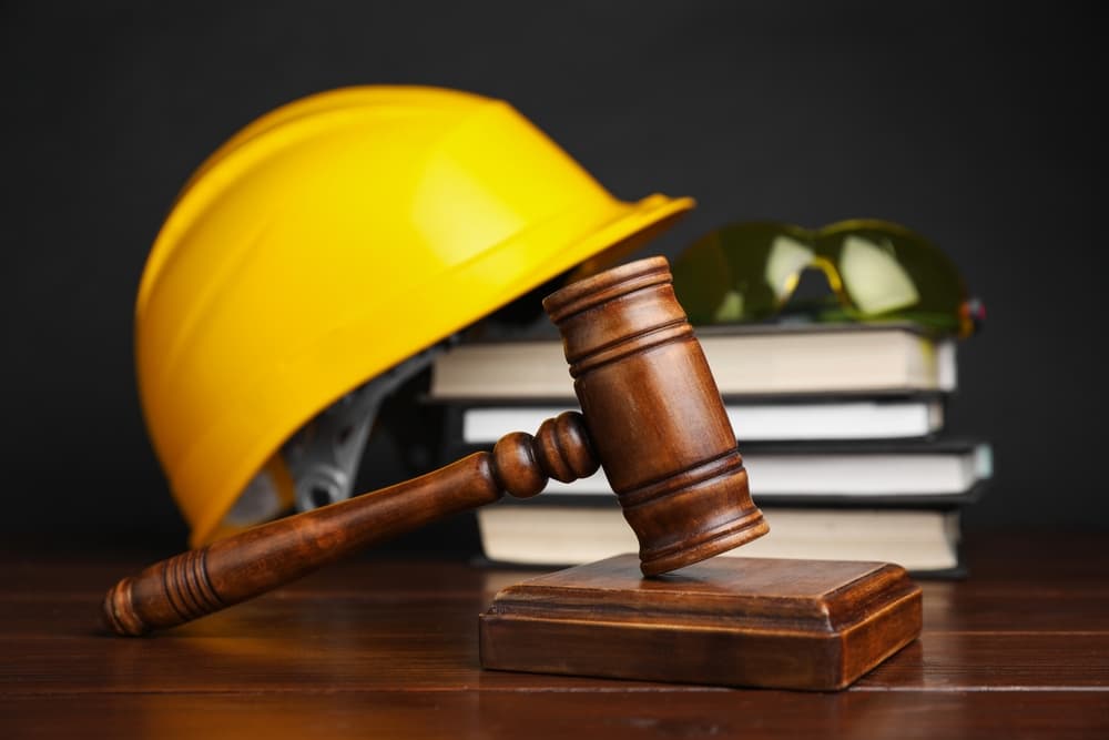 Accident at work concept. Gavel, books and construction worker's protective gear on wooden table, selective focus