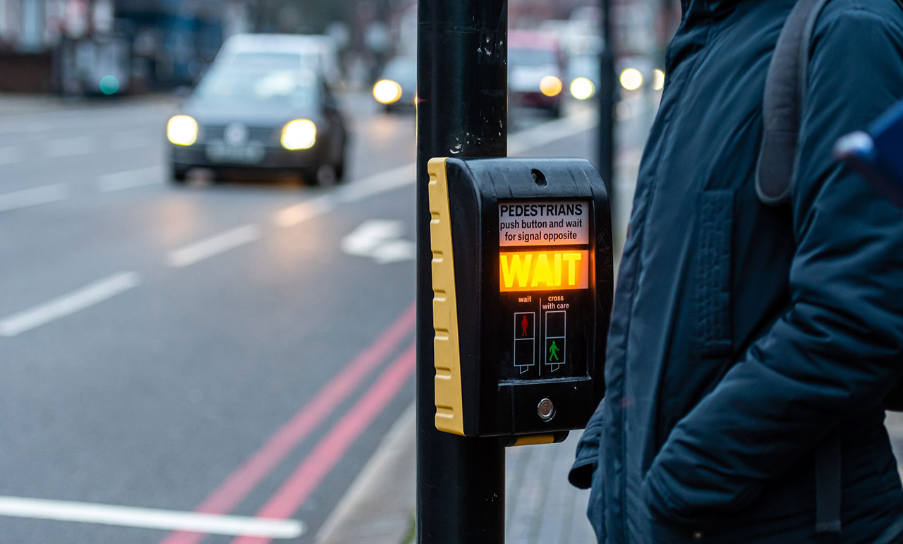 Yellow pedestrian crossing push button with WAIT instruction on a street pole, representing crosswalk signal control and pedestrian accident liability