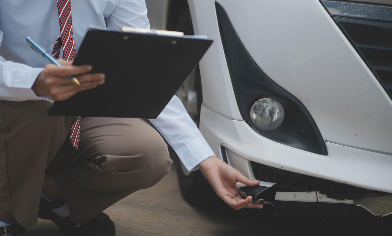 Insurance agent writing on a clipboard while examining a damaged car, representing appraisal evidence used to support a diminished value claim