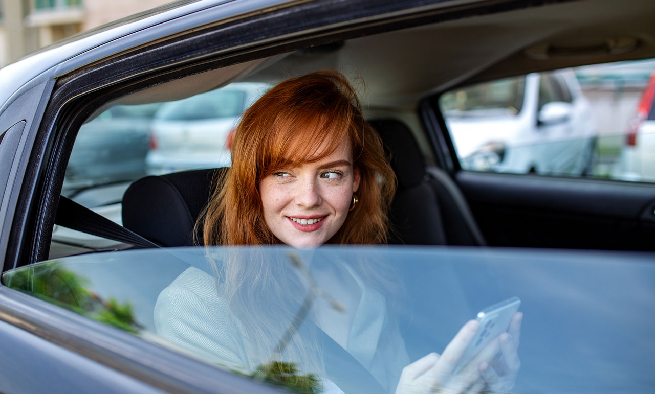 Passenger using a smartphone in the back seat of a car, concept image representing Uber and Lyft accident claims and rideshare insurance coverage.